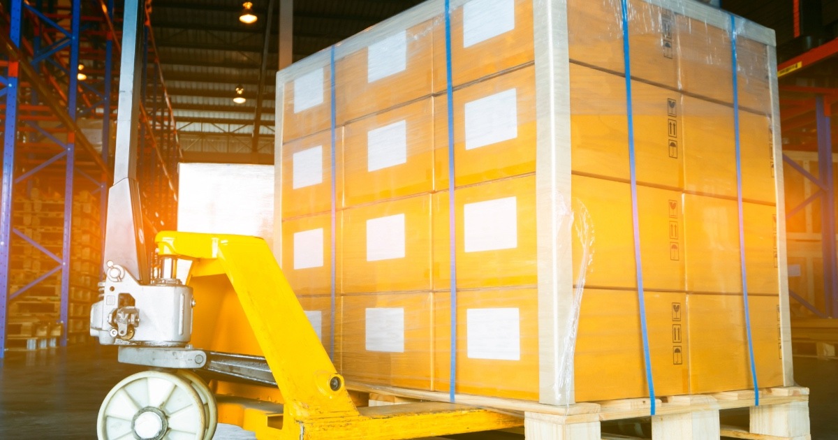 Kuva varastosta, jossa paljon laatikoita pumppukärryn päällä